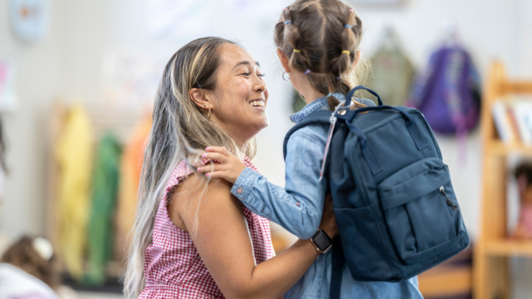 Child with a backpack saying hello to a woman.